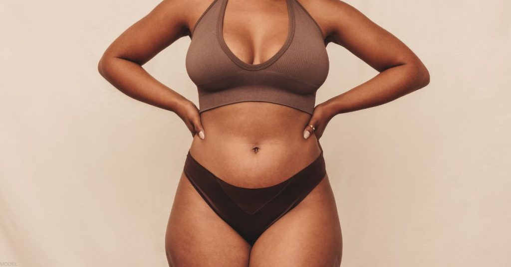 Woman’s midsection showing natural body contours, wearing a sports bra and underwear.